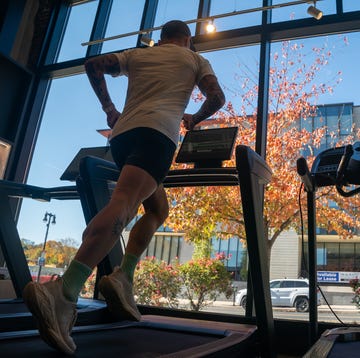 person jogging on a treadmill inside a gym with a view of autumn trees through large windows